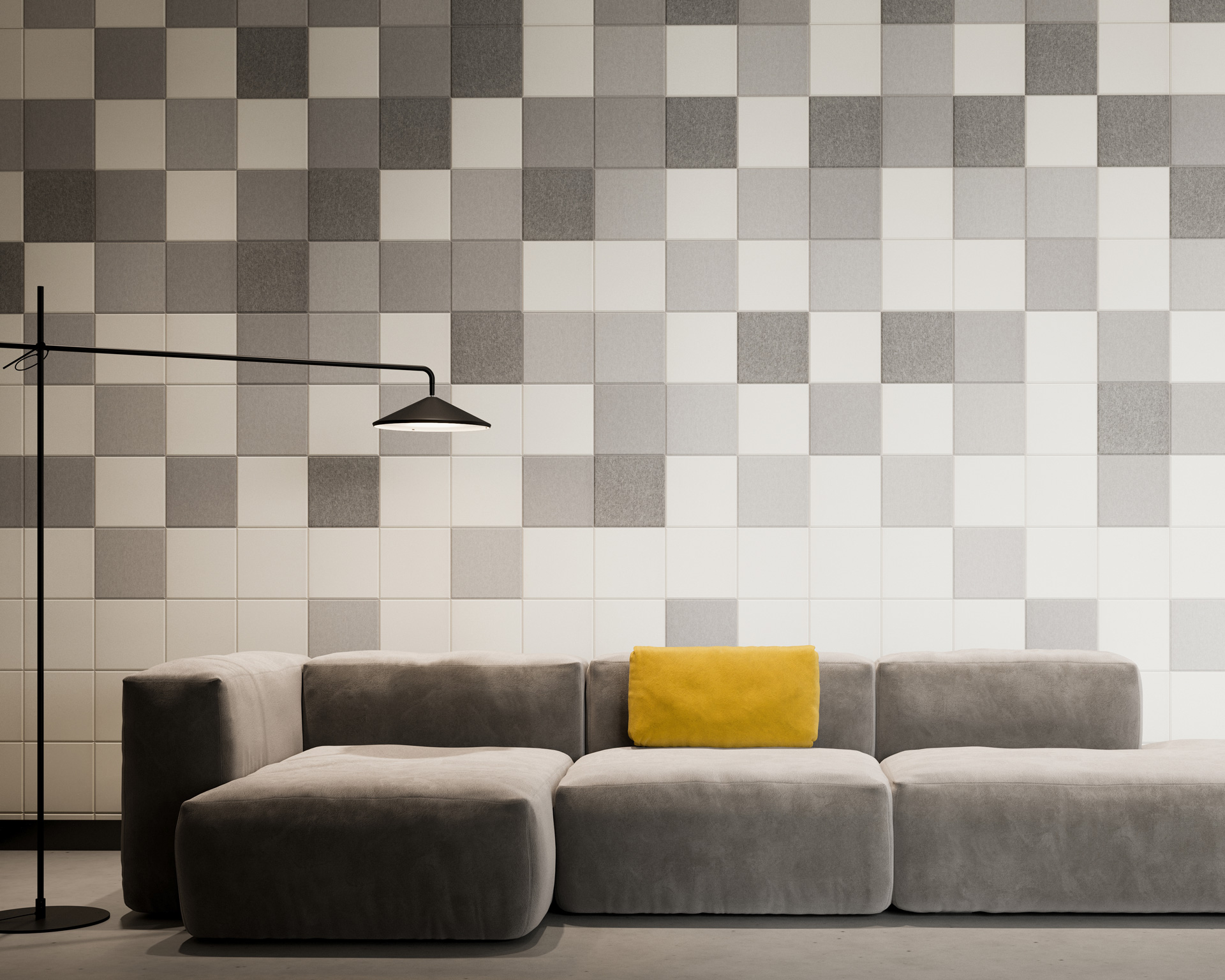 A modern living room features a large, plush gray sofa with a single yellow cushion. Behind the sofa, the wall is adorned with a grid of acoustic felt wall tiles in a checkered pattern of gray and white. A sleek, black floor lamp with an angular design stands next to the sofa.
