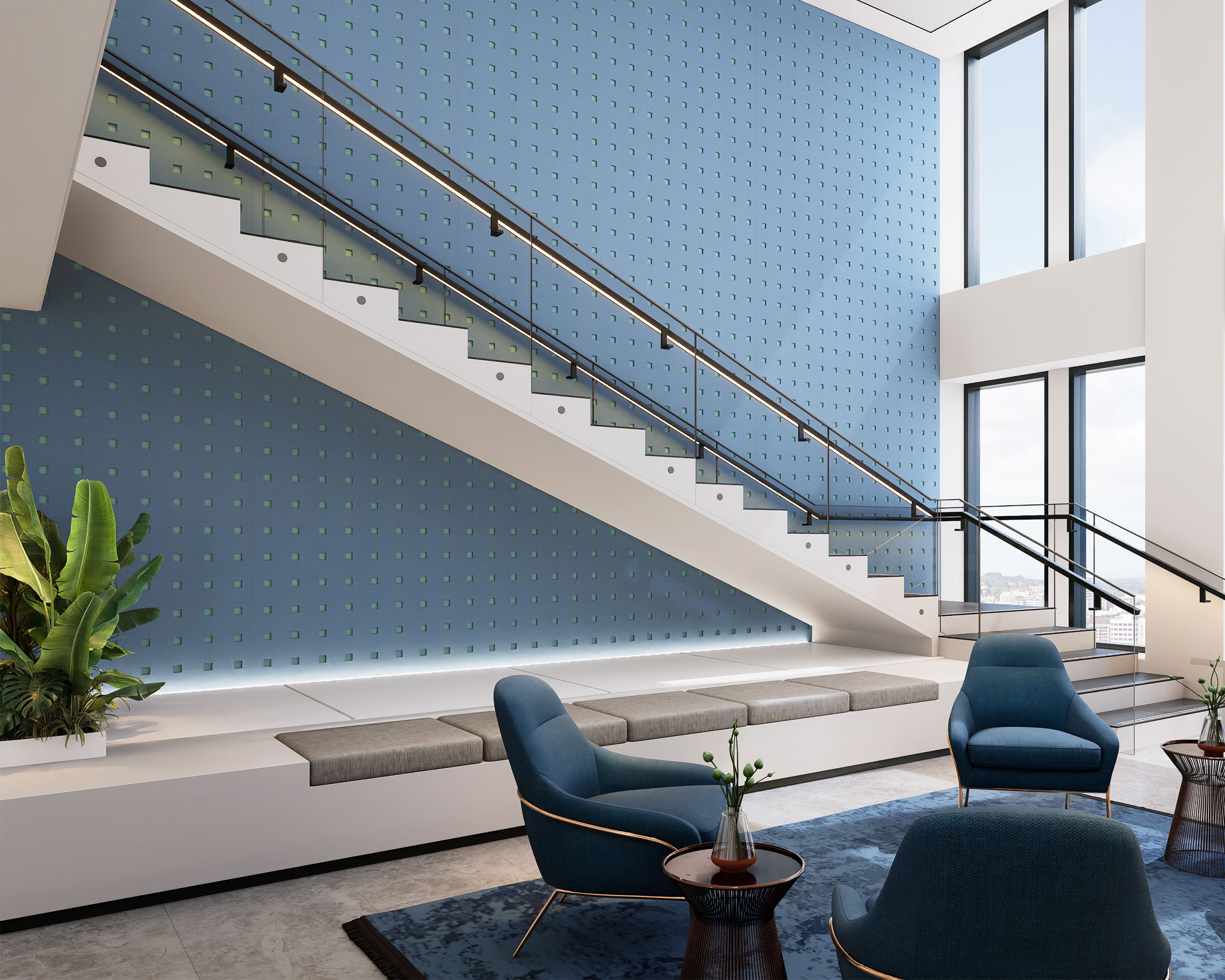 A modern indoor lounge area features a tall staircase with blue, textured square acoustic felt wall panels and a glass railing. Blue chairs and small tables are arranged on a blue rug, while a large plant adds greenery to the space. The area is brightly lit by large windows.