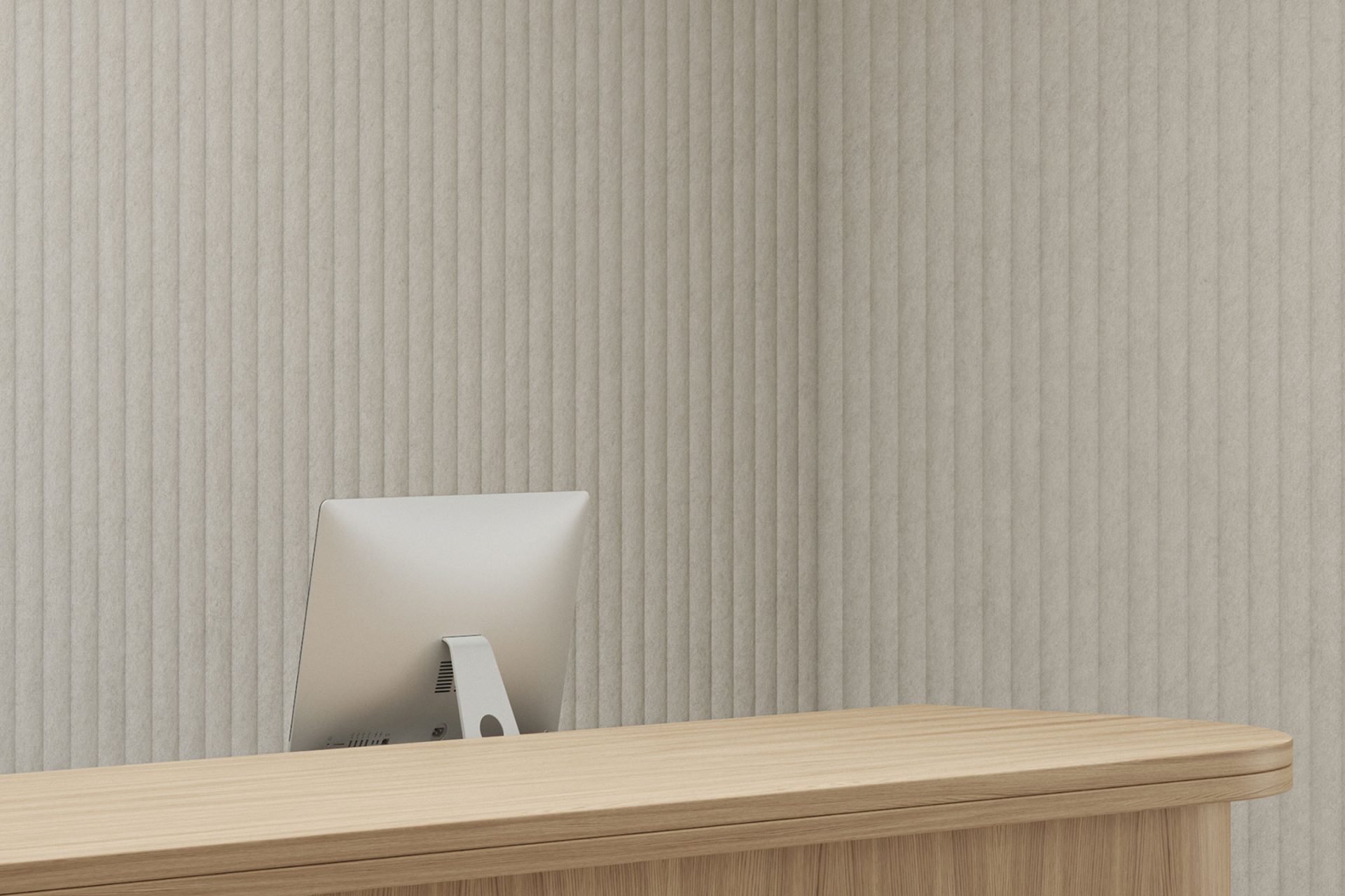 A minimalist reception desk with a wooden surface is in front of a light gray, vertically textured wall featuring celestial acoustic felt wall panels. An iMac computer is the only item on the desk, facing towards the potential receptionist's side, creating a clean and uncluttered workspace.