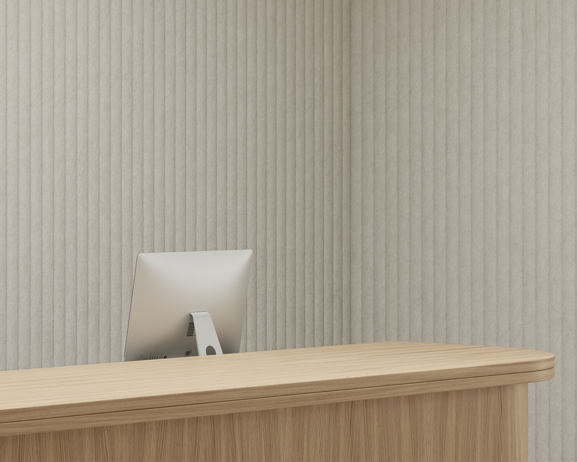 A minimalist reception desk with a wooden surface is in front of a light gray, vertically textured wall featuring celestial acoustic felt wall panels. An iMac computer is the only item on the desk, facing towards the potential receptionist's side, creating a clean and uncluttered workspace.