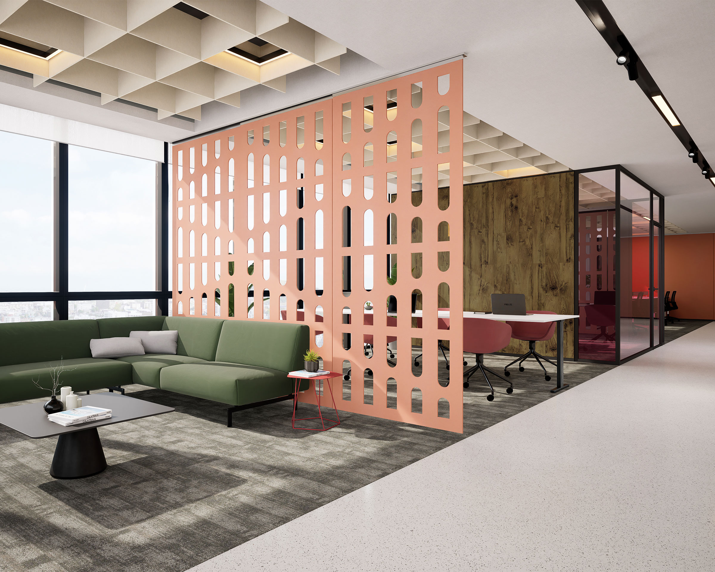 A modern office space with a green sectional sofa and a black coffee table on a gray carpet. A pink acoustic felt screen with geometric cutouts divides the lounge from a workspace with desks and red chairs. Large windows offer natural light, and the ceiling features a grid design.