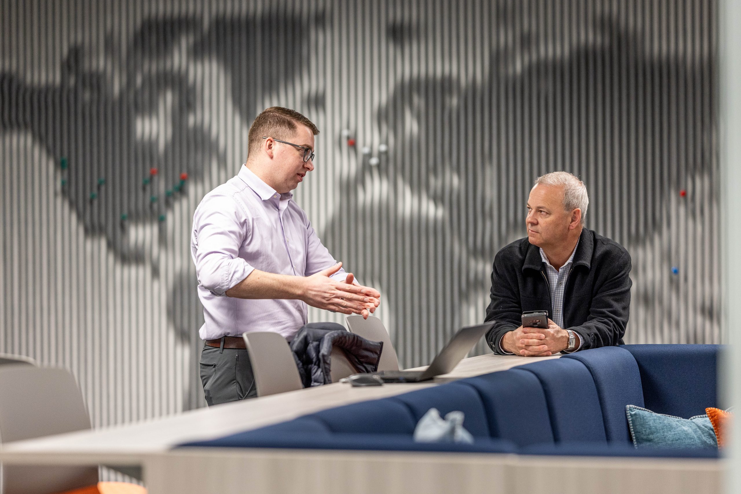 Two employees having a conversation in front of a map of Acoufelt global locations.