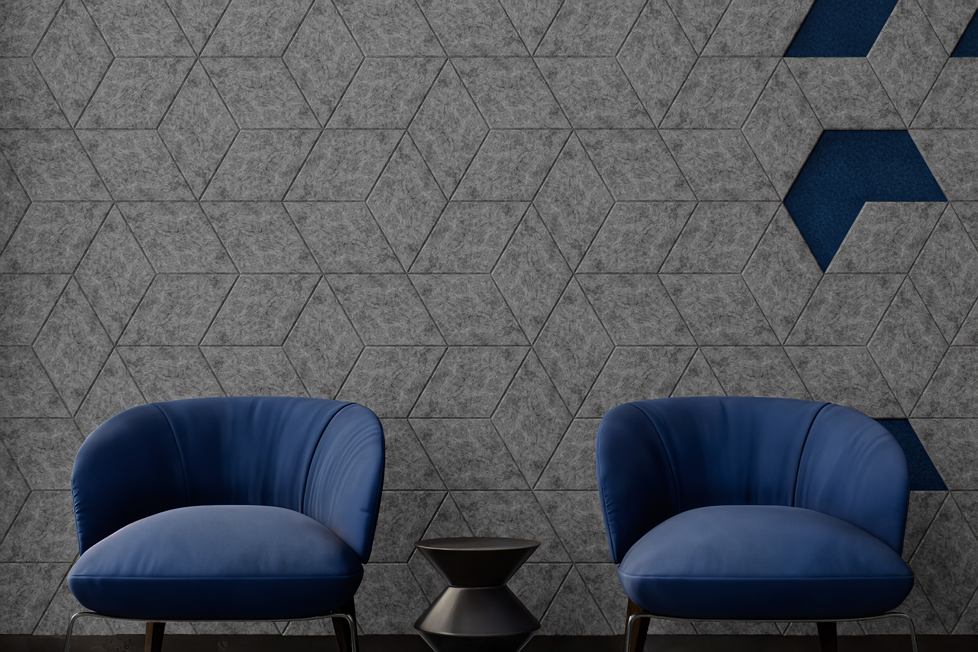 Two blue armchairs sit against a geometric-patterned wall with gray diamond acoustic felt tiles and blue accents. Between the chairs is a small, black, hourglass-shaped side table. The minimalist setting emphasizes the modern and sleek design.
