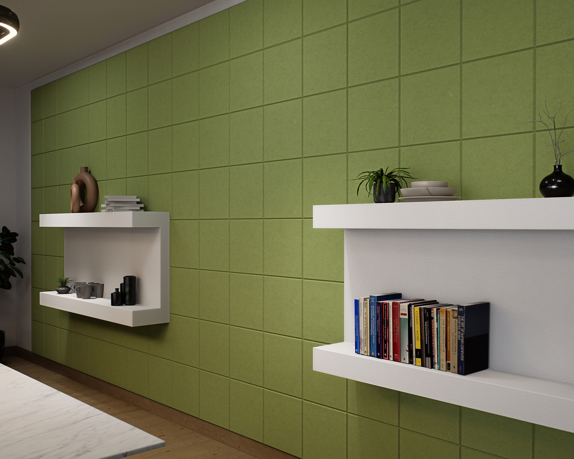 A modern interior with a green acoustic felt tiled accent wall featuring two white floating shelves. The top shelf holds decorative items including plants and vases, while the bottom shelf displays books and additional decorations. A small corner of a white marble table is visible.
