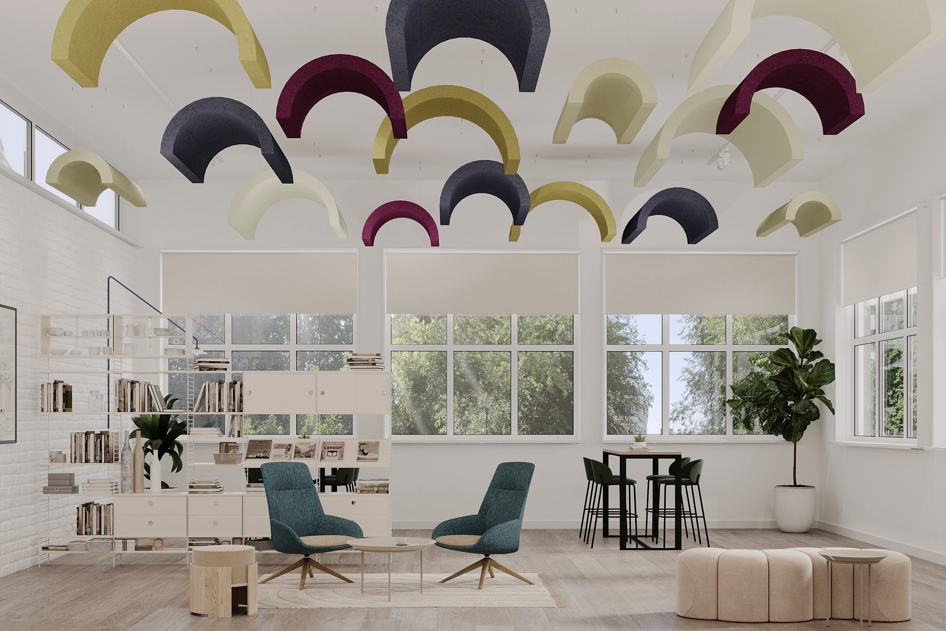 A bright, modern office space with large windows, light-colored floors, and white walls. Colorful curved acoustic felt clouds hang from the ceiling. The room features teal chairs, a wooden coffee table, bookshelves, an indoor plant, and a set of poufs and a table.