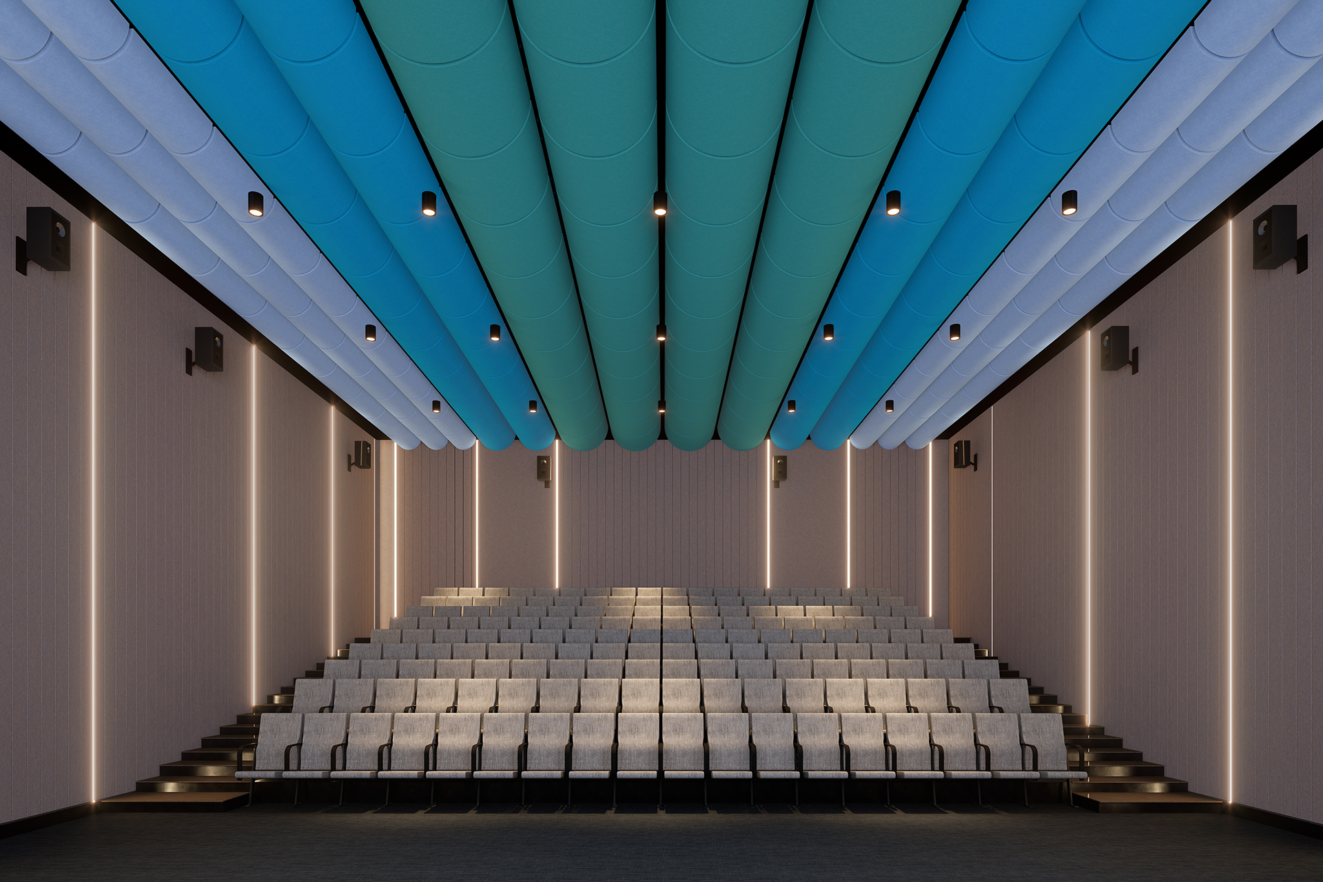 An empty, modern lecture hall with tiered seating facing the front. The ceiling has blue, cylindrical acoustic felt clouds, and the walls are equipped with speakers. Steps on either side lead to the rows of seats. The hall is well-lit with recessed lighting.