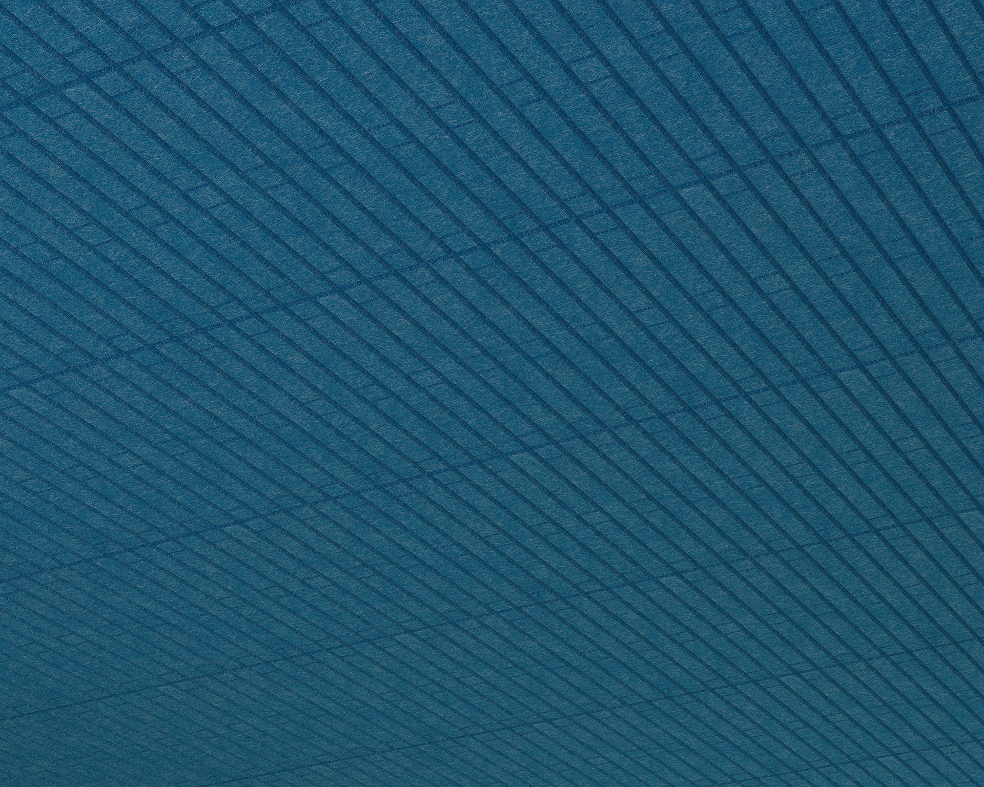 A close-up view of an acoustic felt textured surface with parallel, diagonal lines forming a grid-like pattern. The blue-toned design evokes the cozy tranquility of a cabin, as light and shadow play across its surface, adding depth and dimension.