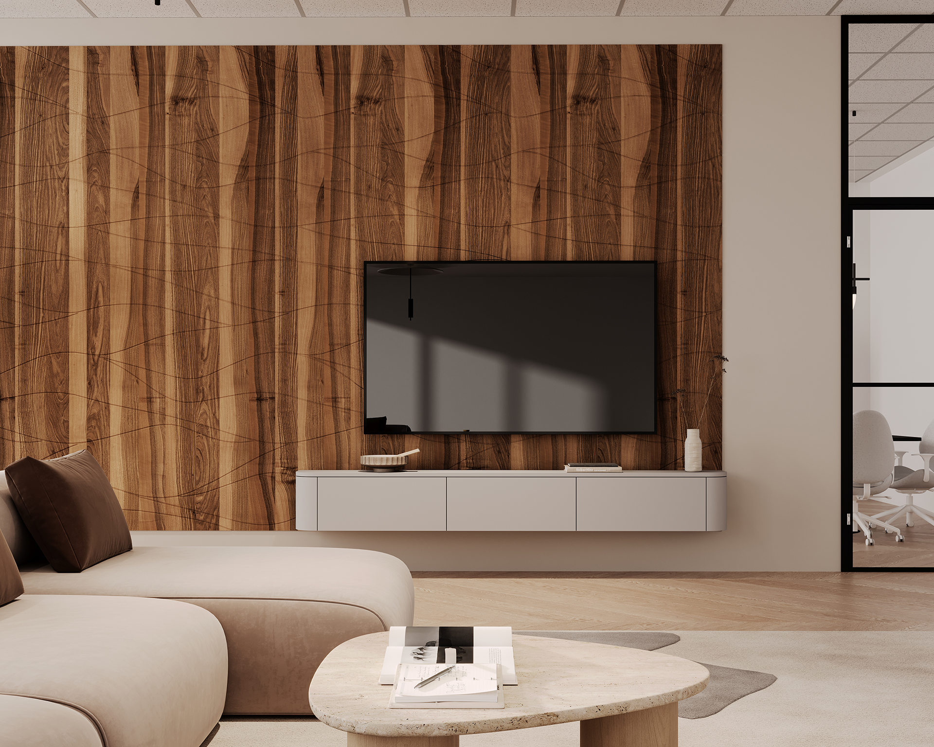 A modern living room featuring a large flat-screen TV mounted on a woodgrain acoustic felt wall. A sleek white console holds a few decor items. A beige sectional sofa and a round coffee table are in the foreground. An office space is visible through a glass wall.