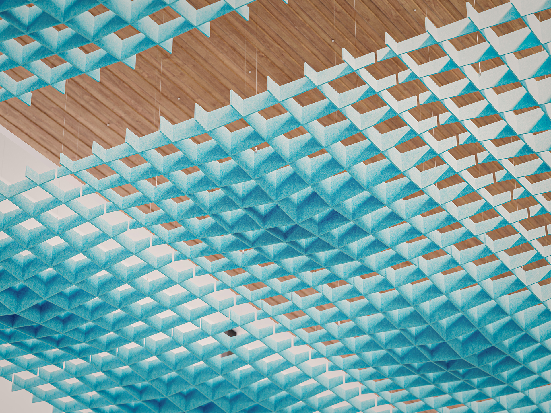 An acoustic felt ceiling installation of blue, grid-like panels hangs beneath a wooden ceiling, creating a geometric pattern with a modern, airy appearance.