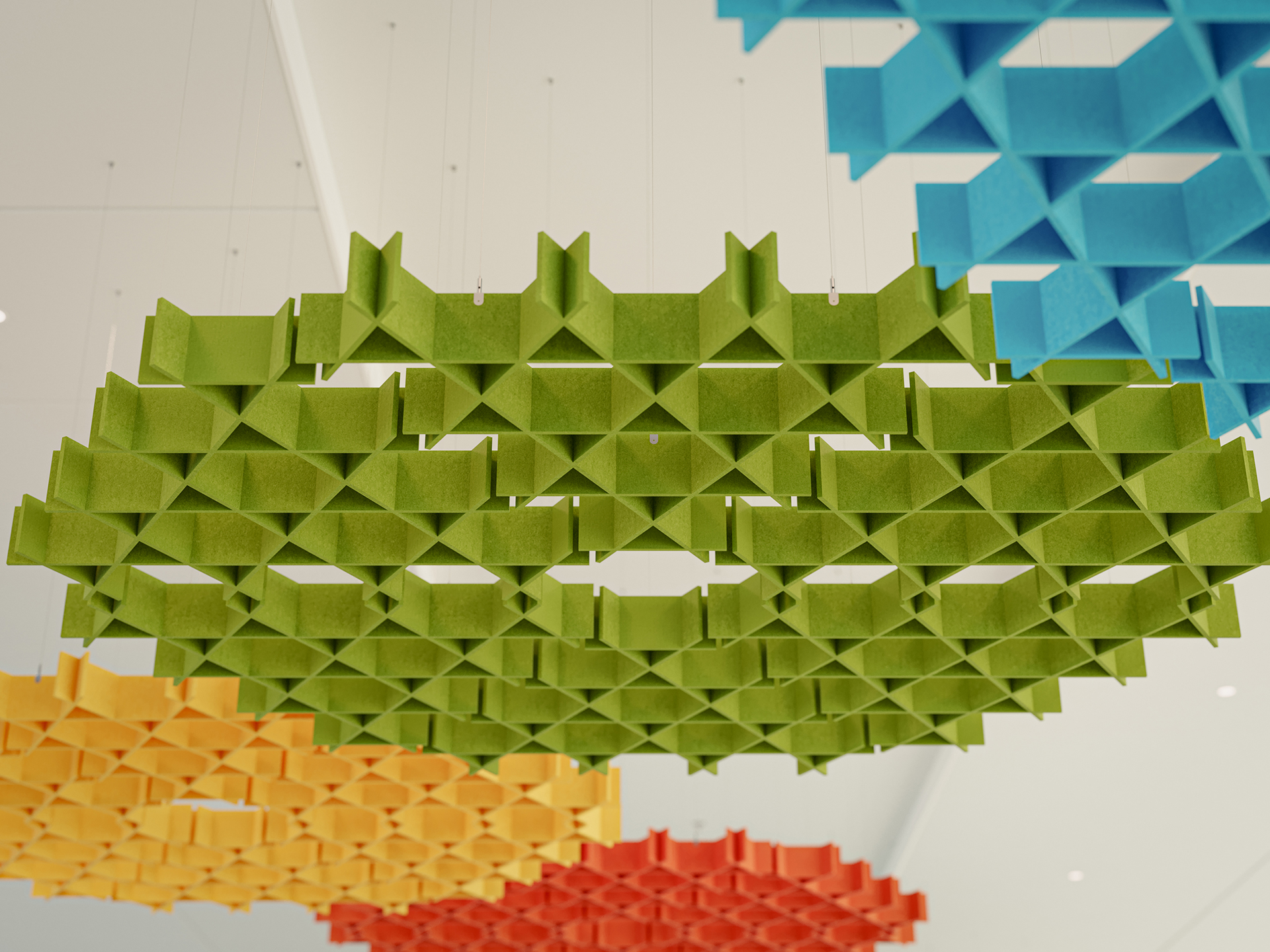 Colorful geometric acoustic felt clouds hang from a white ceiling. The structures are circular, made of interlocking pieces in green, yellow, orange, red, and blue, creating a modern, artistic installation.