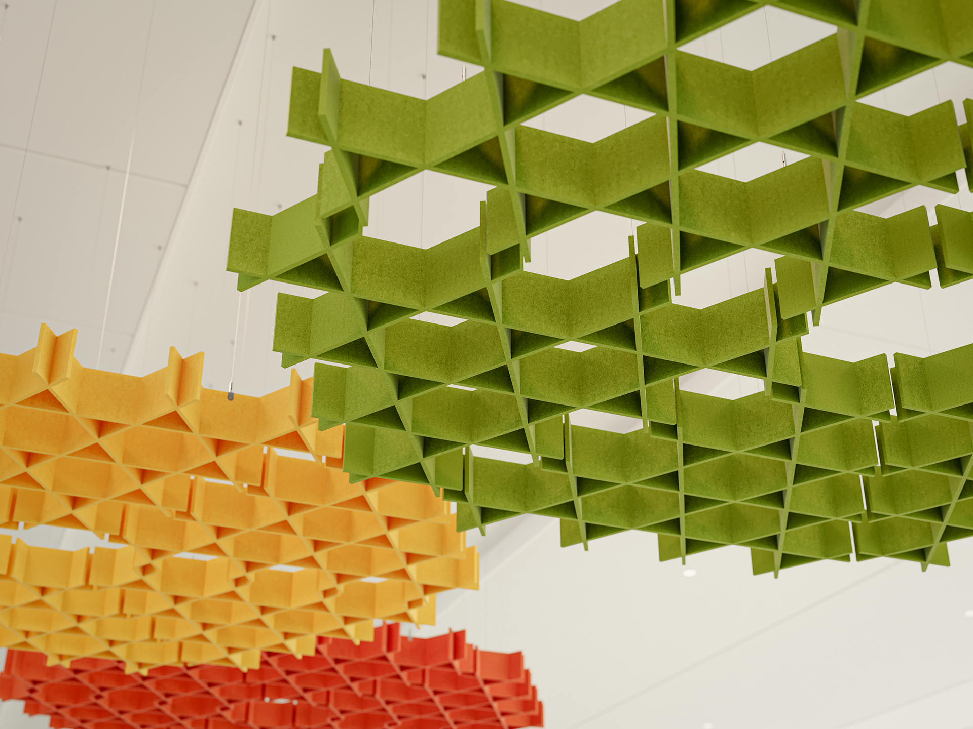 Geometric acoustic felt ceiling panels in green, yellow, and red hang from a white ceiling. The panels have a grid-like, interlocking pattern and add a colorful, modern touch to the interior space.