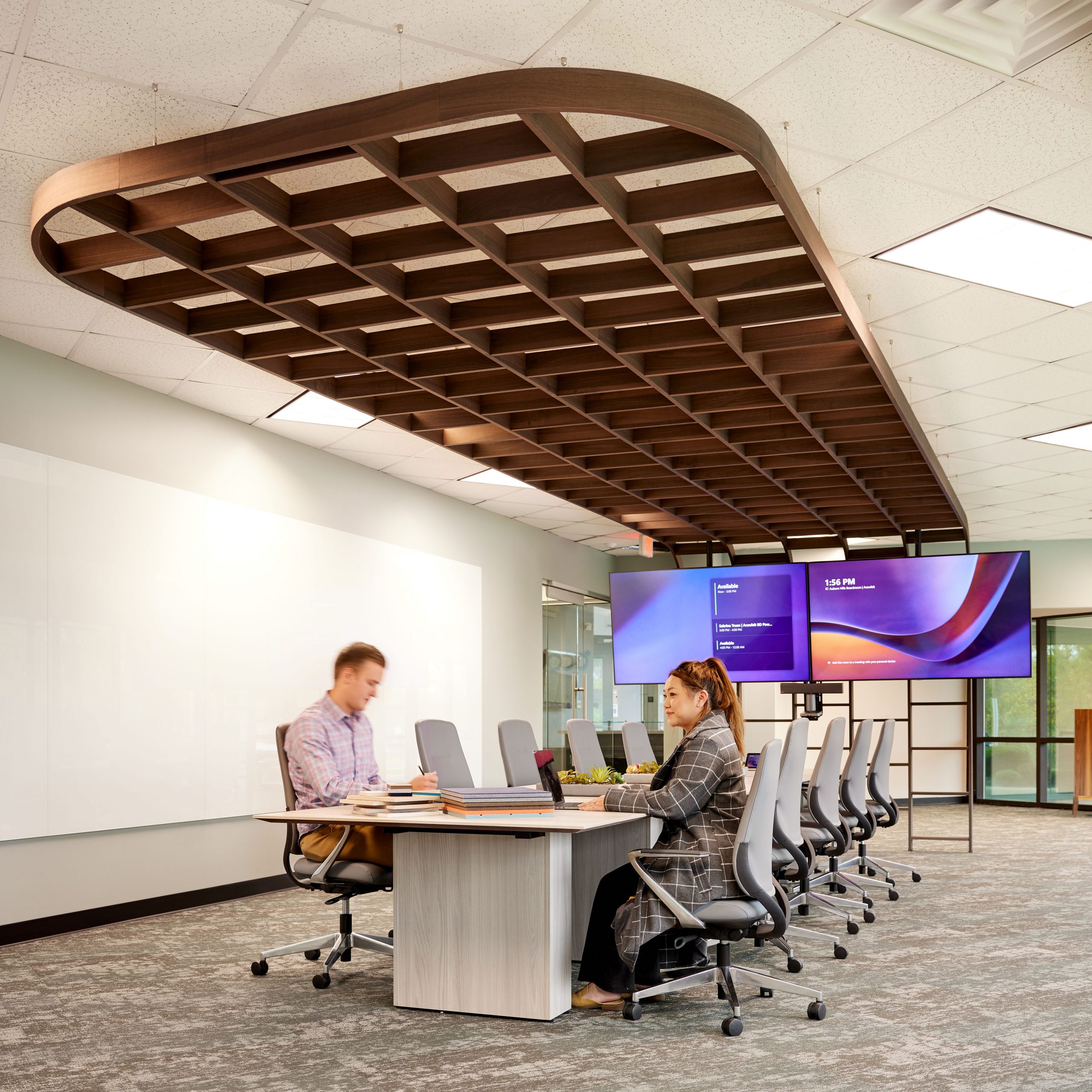 Two people sitting at a conference table with wood felt trellis overhead