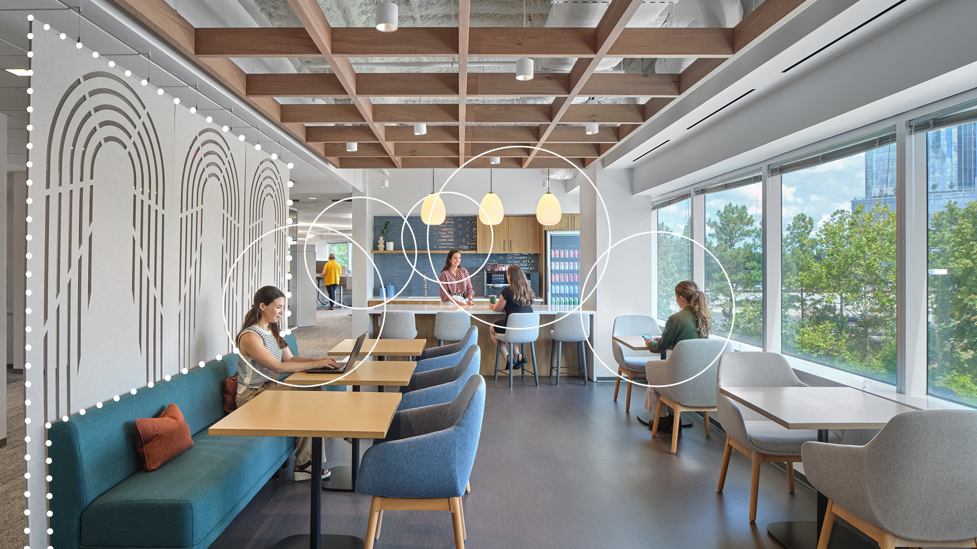 Modern office lounge with large windows, people sitting at tables and on sofas working or talking, wood-beam acoustic ceiling grid, decorative acoustic felt partition, pendant lights, and greenery visible outside.